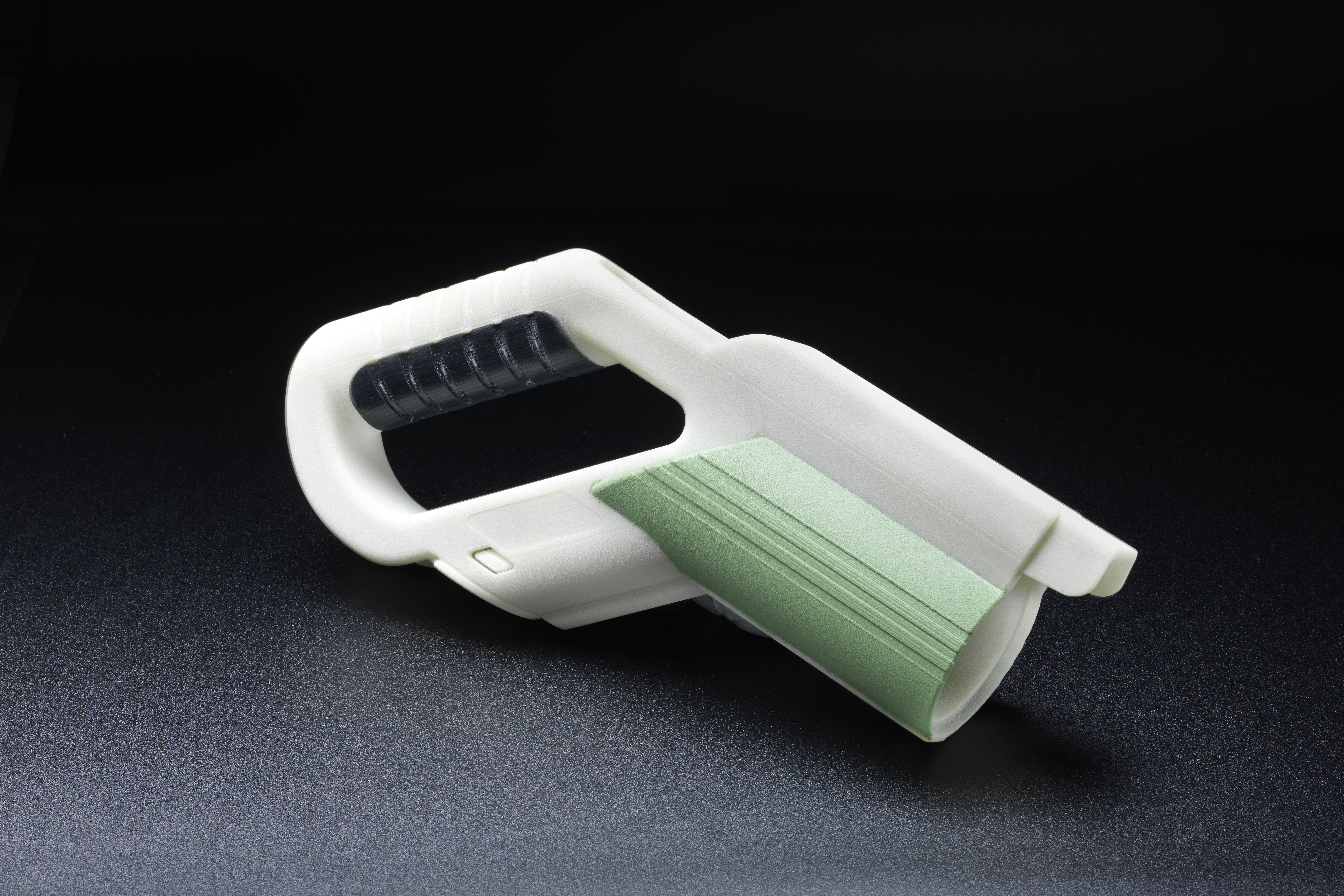 Manico in plastica bianca con impugnatura nera e parte in plastica verde a coste, su sfondo nero.